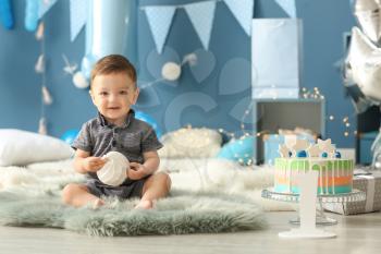Cute little boy sitting on fluffy rug in room decorated for birthday party�