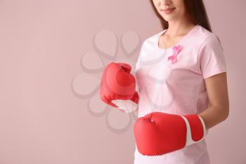 Beautiful woman with pink ribbon and boxing gloves on color background. Breast cancer concept�