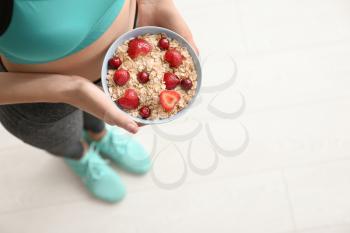Young woman with bowl of tasty oatmeal after training indoors�