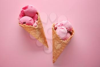 Waffle cones with delicious strawberry ice-cream on color background�
