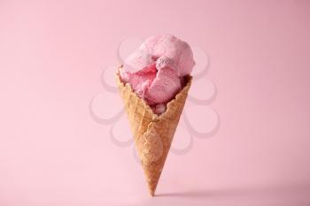 Waffle cone with delicious strawberry ice-cream on color background�