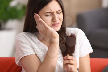 Young woman with sensitive teeth and cold ice cream on sofa at home�