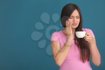 Young woman with sensitive teeth and cup of hot coffee on color background�
