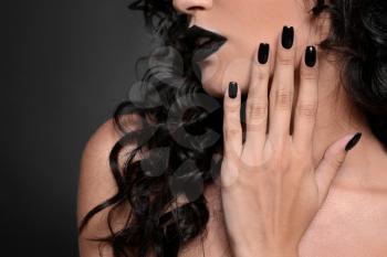 Fashionable young woman with black manicure on dark background, closeup�