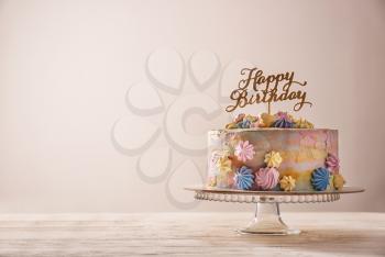 Stand with delicious birthday cake on table against light background�