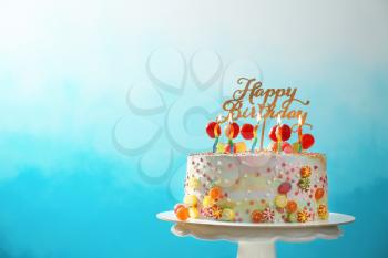 Stand with beautiful tasty birthday cake on color background�