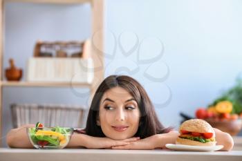 Woman with tasty burger and fresh salad indoors. Choice between healthy and unhealthy food�