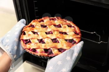 Woman taking freshly baked cherry pie out of oven, closeup�