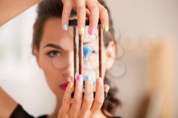 Young woman with colorful manicure holding hourglass, closeup�