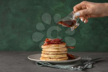 Woman pouring maple syrup onto tasty pancakes with fried bacon�