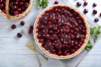 Tasty homemade pie and basket with ripe cherries on white wooden table�