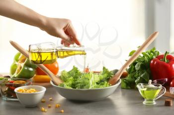 Woman adding olive oil to fresh vegetable salad on table�