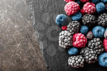 Slate plate with delicious frozen berries on grey background�