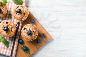 Wooden board with tasty blueberry muffins on table�