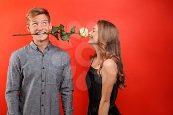 Young man holding beautiful flower for his beloved girlfriend in mouth on color background�