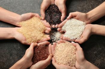 Women holding different types of rice on grey background, top view�
