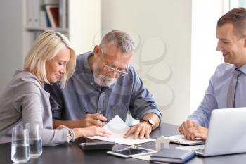 Mature couple signing document in estate agent's in office�