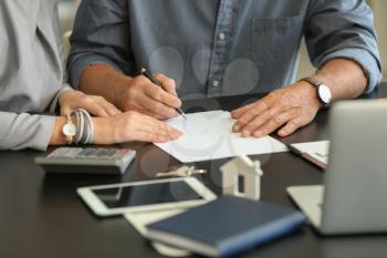 Mature couple signing document in estate agent's office�