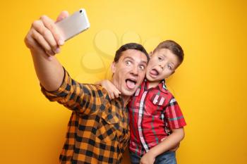 Little boy and his dad taking funny selfie on color background�