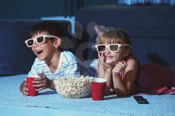 Cute children in 3d glasses watching movie on carpet in evening�