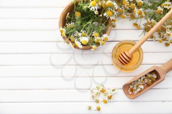 Jar of honey with chamomile flowers on wooden table�