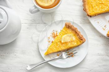 Plate with piece of tasty lemon pie and cup of tea on white wooden table�