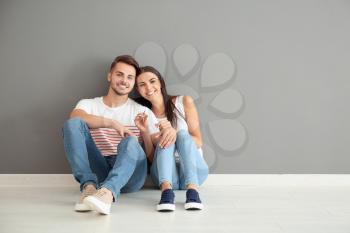 Young happy couple with key sitting on floor at new home�