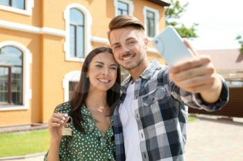 Young happy couple taking selfie with key of their new house outdoors�