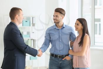 Young man shaking hands with estate agent in office�