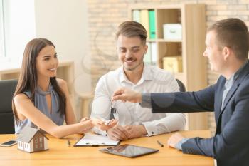 Real estate agent giving key of new house to young couple in office�