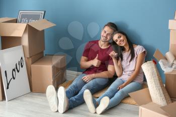 Young happy couple with key and moving boxes sitting on floor at new home�