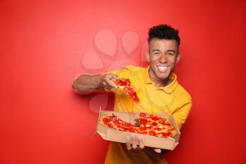 Young African-American man eating delicious pizza on color background�