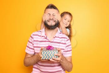 Little girl giving present to her father on color background�