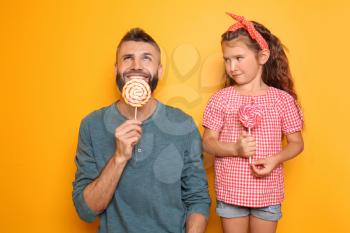 Funny portrait of father and his little daughter with lollipops on color background�