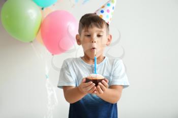 Cute little boy making a wish and snuffing out candle on Birthday cake against light background�