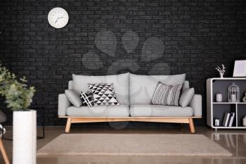 Interior of living room with stylish comfortable sofa near black brick wall�