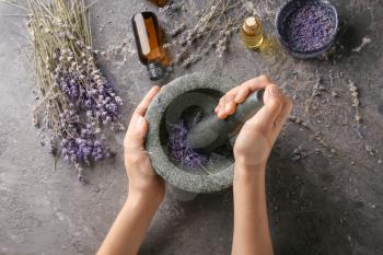 Woman grinding lavender flowers in mortar, top view�