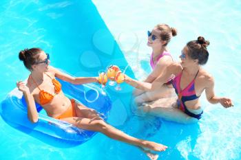 Beautiful young women drinking cocktails in swimming pool on summer day�