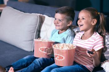 Children eating popcorn while watching TV in evening�