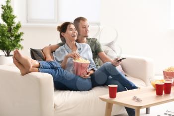Couple eating popcorn while watching TV at home�
