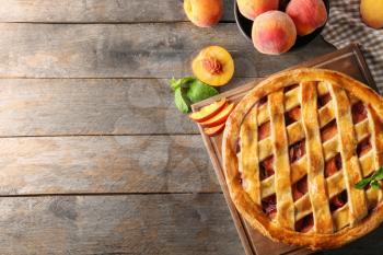 Board with delicious peach pie on wooden table�