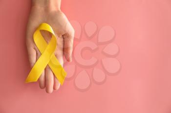 Woman holding yellow ribbon on color background. Cancer awareness concept�