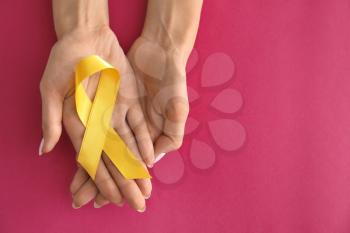 Woman holding yellow ribbon on color background. Cancer awareness concept�