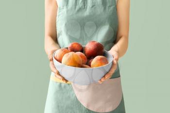 Woman holding bowl with fresh peaches on color background�