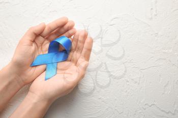 Woman holding blue ribbon on light background. Cancer concept�
