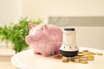 Thermostat, piggy bank and coins on table at home. Heating saving concept�