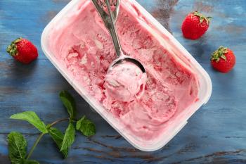 Container with delicious strawberry ice-cream on wooden background 
