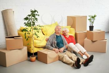 Mature couple sitting on floor near boxes and sofa after moving into new house�
