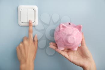 Woman with piggy bank switching off the light. Electricity saving concept�