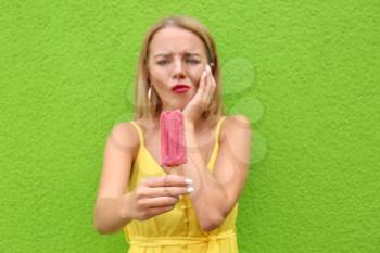 Beautiful young woman with sensitive teeth and cold ice cream near color wall�